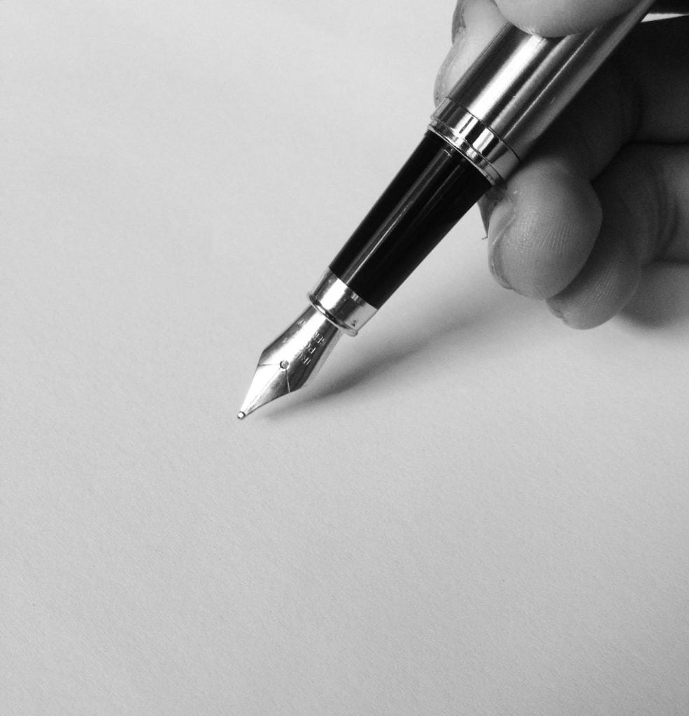 A person holding a fountain pen with a shiny metal tip poised over a blank sheet of paper. The image is in black and white, emphasizing the sleek, classic design of the pen and the smooth texture of the paper, perhaps ready to draft crucial documents on international arbitration errors.