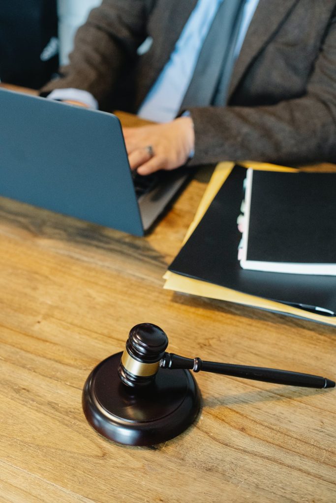 A person in formal attire is working on a laptop. The desk features a gavel and striking block, suggesting a legal context, along with folders and papers, likely related to international arbitration cases and errors.