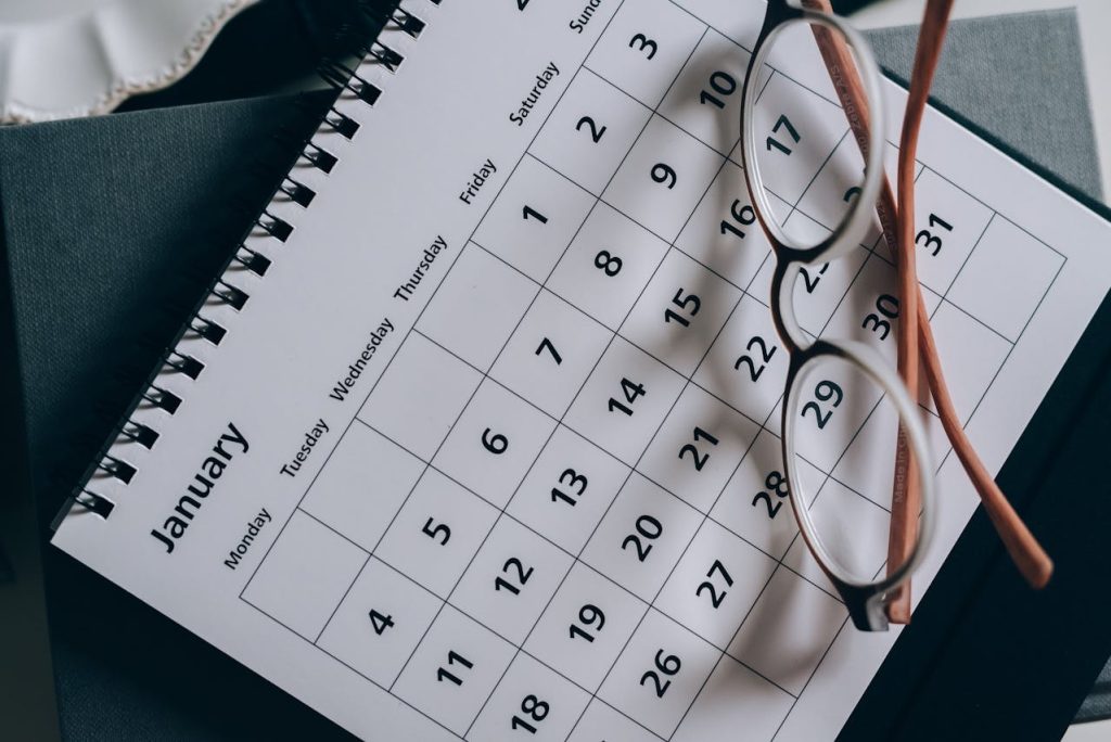 A spiral-bound calendar open to January with dates seen clearly. The calendar rests on a gray book titled "Limits to Appeals of Arbitral Awards," and a pair of glasses with brown frames is placed on top, slightly askew. The scene is softly lit from the left side.