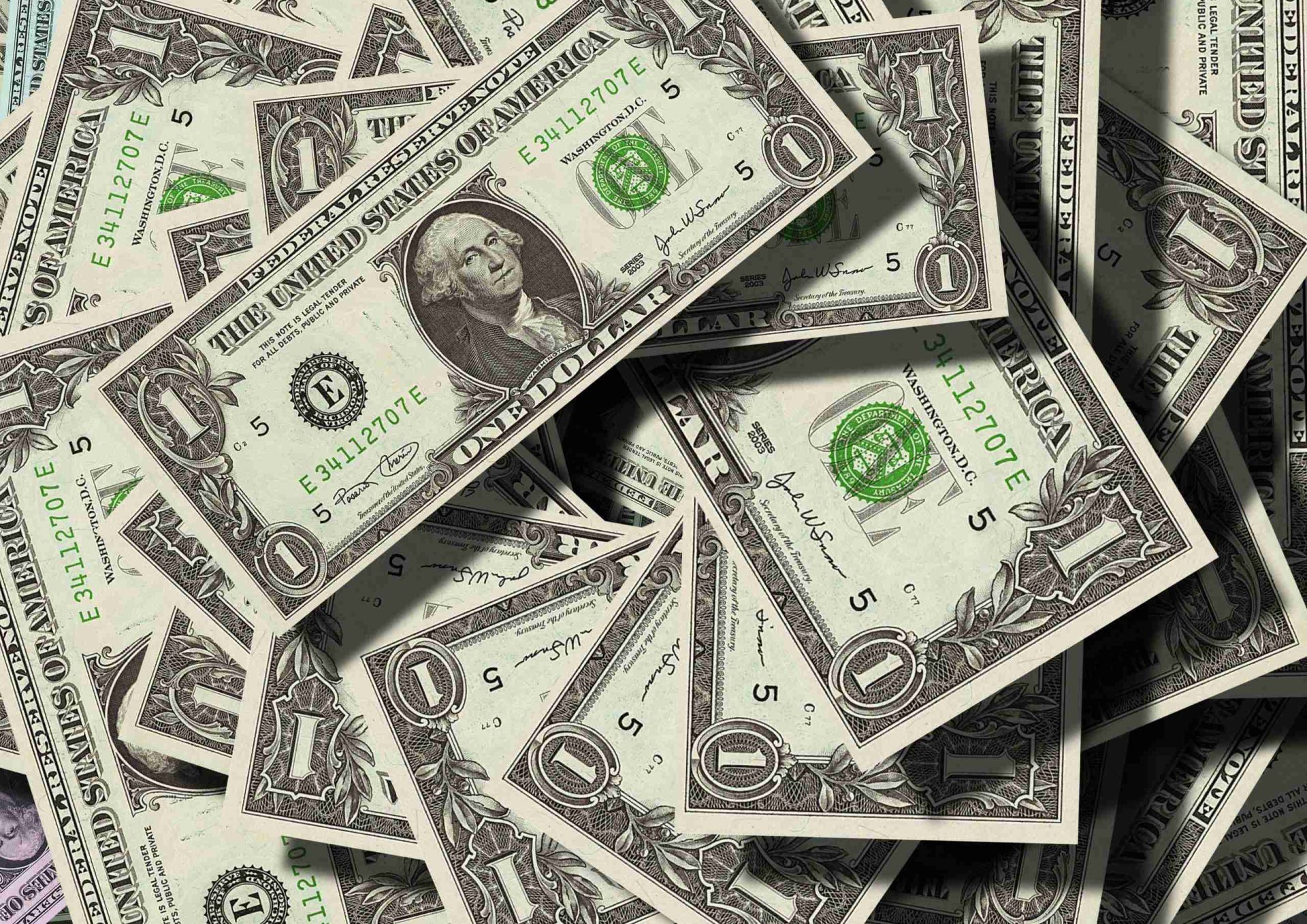 A scattered pile of US one-dollar bills, reminiscent of equitable compensation allowed for breach of an arbitration clause by a third party. The notes, featuring the portrait of George Washington, are overlapping each other and slightly crumpled, creating a textured surface with varying shades of green and white.