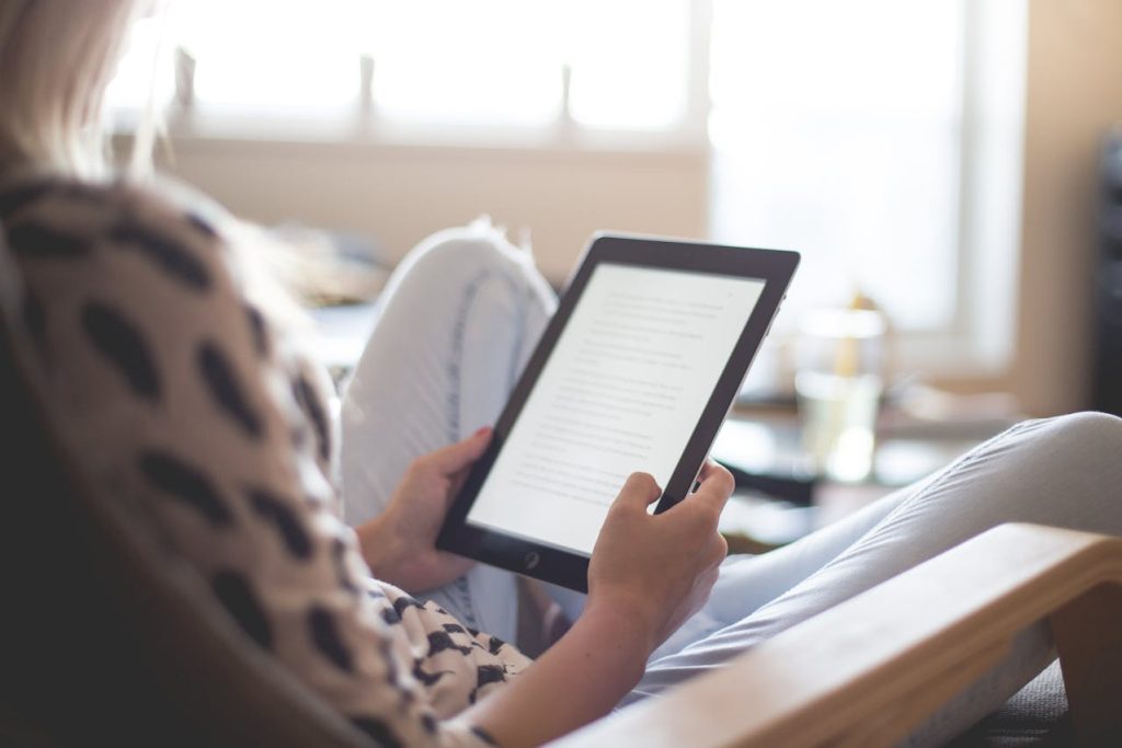 A person sits comfortably in a chair, holding and reading from a tablet that displays an electronic arbitration agreement. They are dressed casually, and the room is softly lit by natural light coming through a window in the background. The scene appears calm and relaxed.